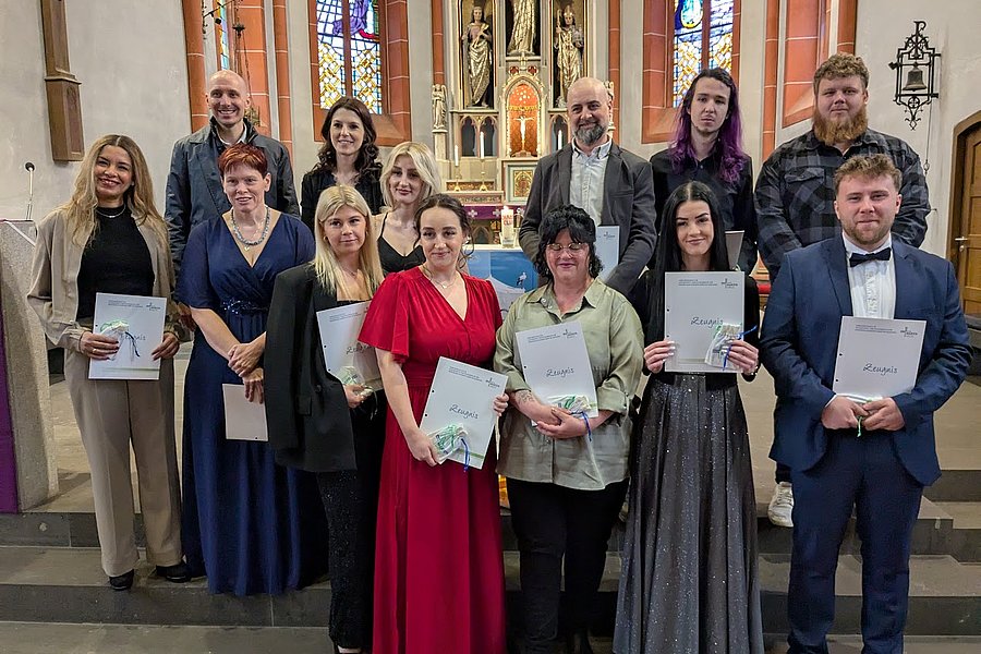 Gruppe von zwölf Personen in festlicher Kleidung steht in einer Kirche, einige halten Urkunden in den Händen