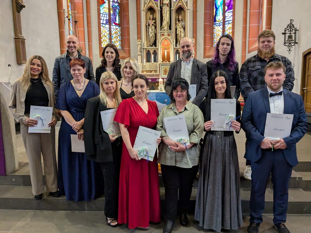 Gruppe von zwölf Personen in festlicher Kleidung steht in einer Kirche, einige halten Urkunden in den Händen