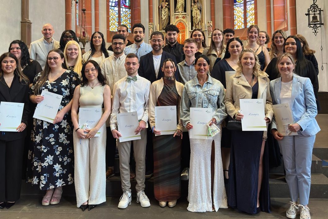 Gruppe von Menschen mit Urkunden in einer Kirche vor Altar und bunten Glasfenstern