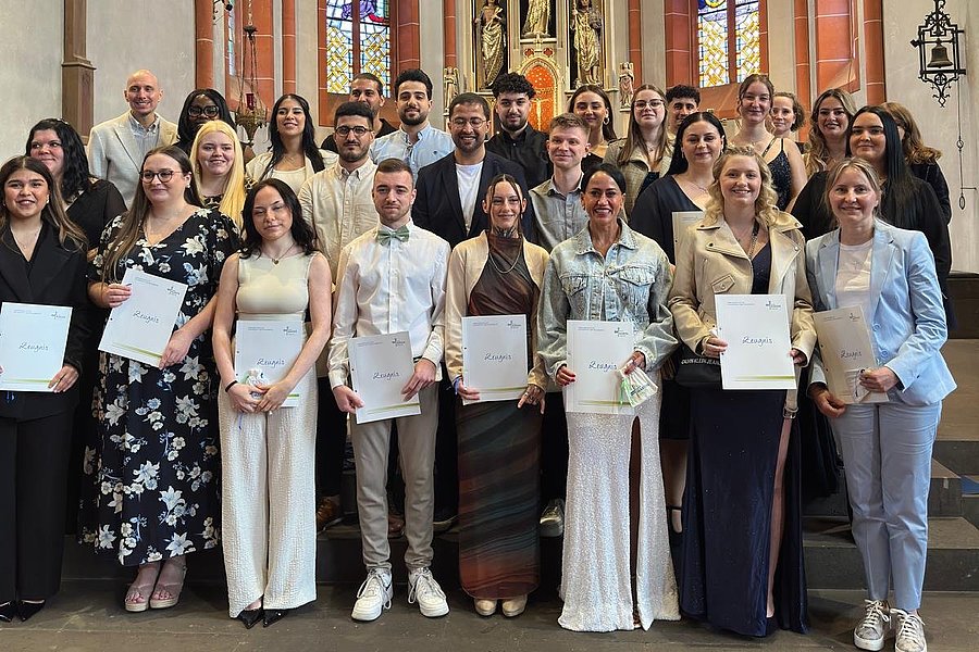 Gruppe von Menschen mit Urkunden in einer Kirche vor Altar und bunten Glasfenstern