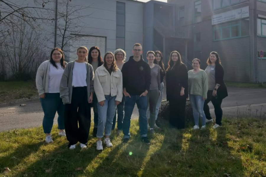 Gruppe von elf Personen steht auf einer Wiese vor einem Gebäude im Hintergrund
